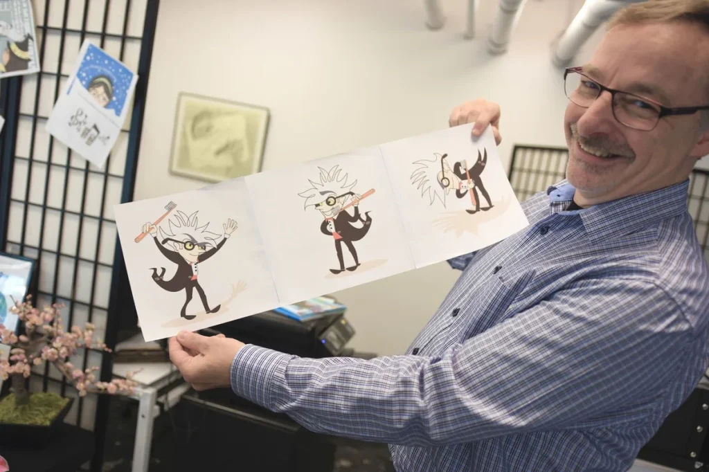 Ken Korber holding illustrations of Maestro character